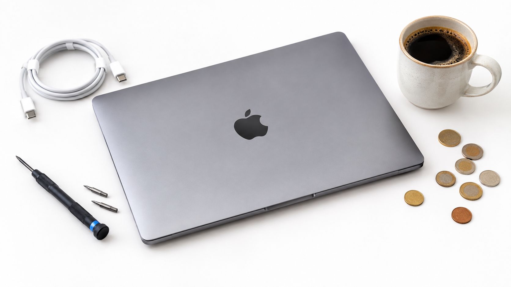 MacBook Pro Sale UK 2026: How to Time and Verify Deals 4 A gray Apple MacBook Pro laptop surrounded by a charging cable, coffee mug, screwdriver, and scattered coins.